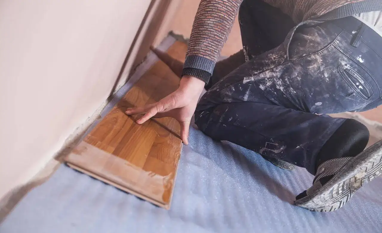 Mano colocando tabla de suelo laminado sobre base aislante.