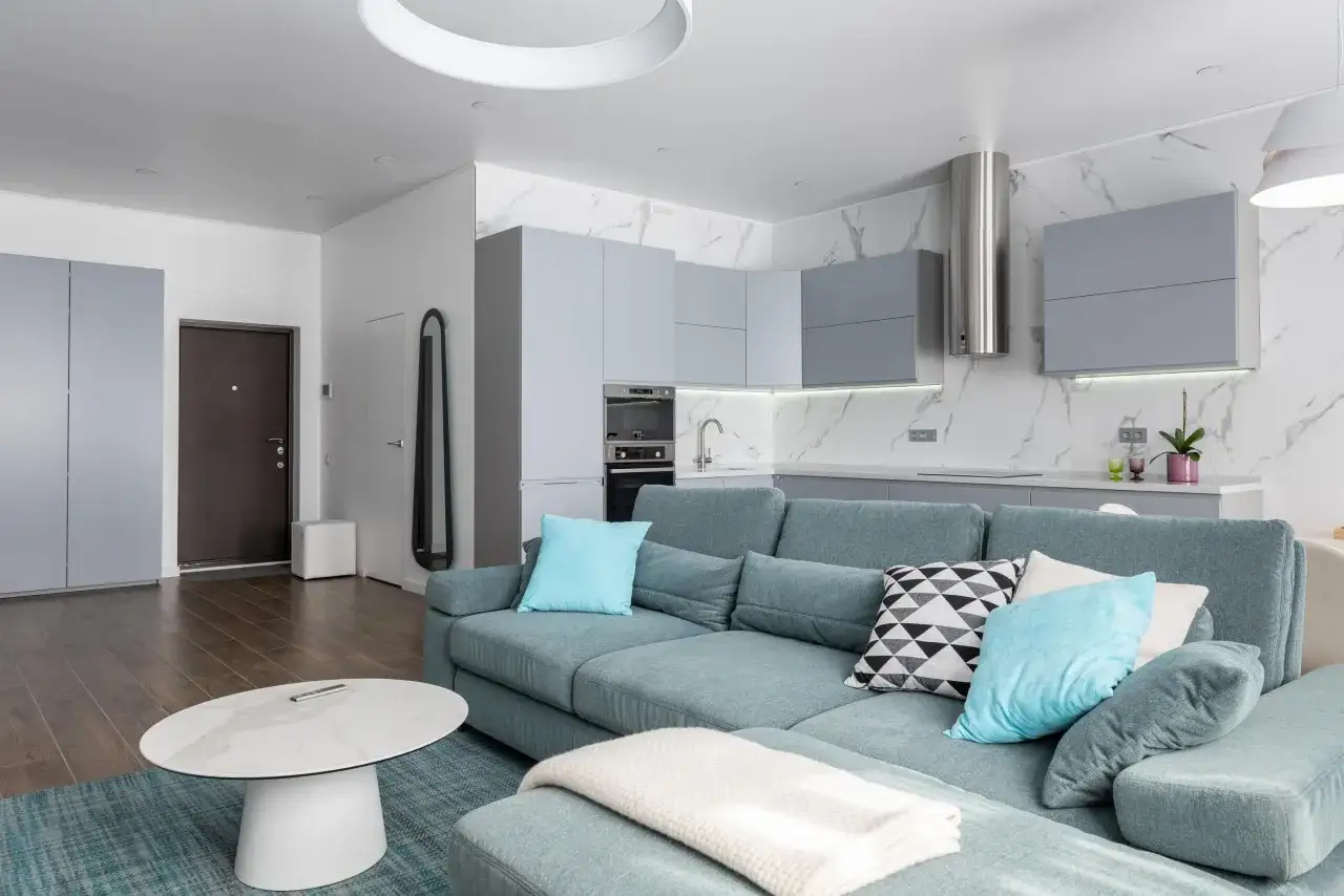 Espaciosa cocina salón comedor de 30 m2 con sofá azul, mesa de centro ovalada y cocina moderna con armarios grises.
