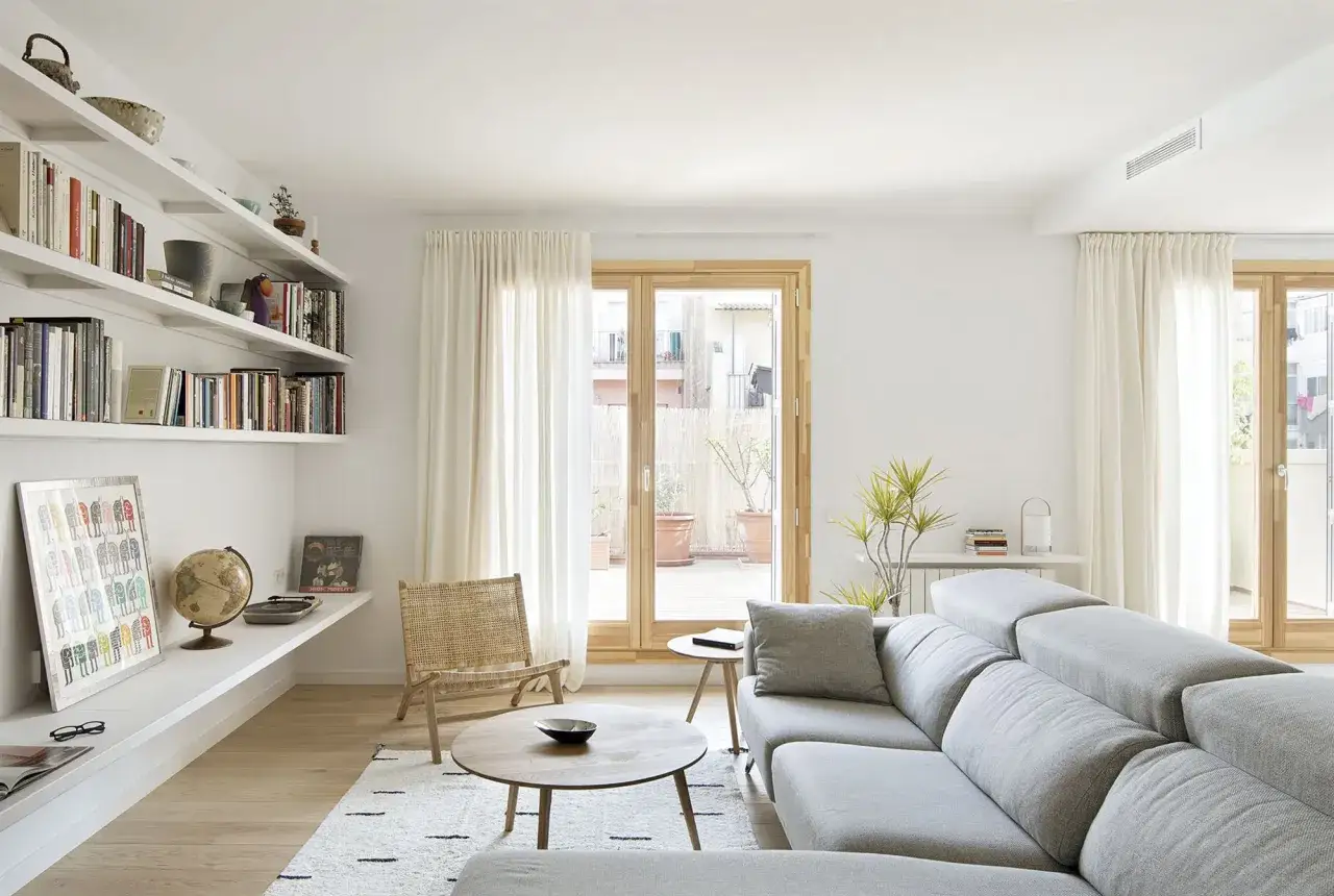 Un salón moderno con estanterías llenas de libros, un sofá gris y una silla de mimbre. Unas sencillas salas pequeñas que invitan a la relajación.