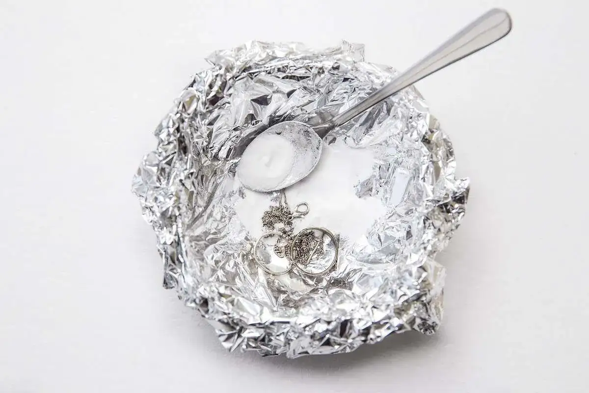 Plata opaca sobre papel de aluminio con bicarbonato y cuchara. Aprende como se limpia la plata en casa.