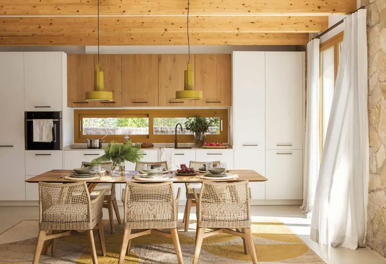Acogedora cocina office con vigas de madera, muebles blancos y de roble, y una mesa de comedor lista para compartir.