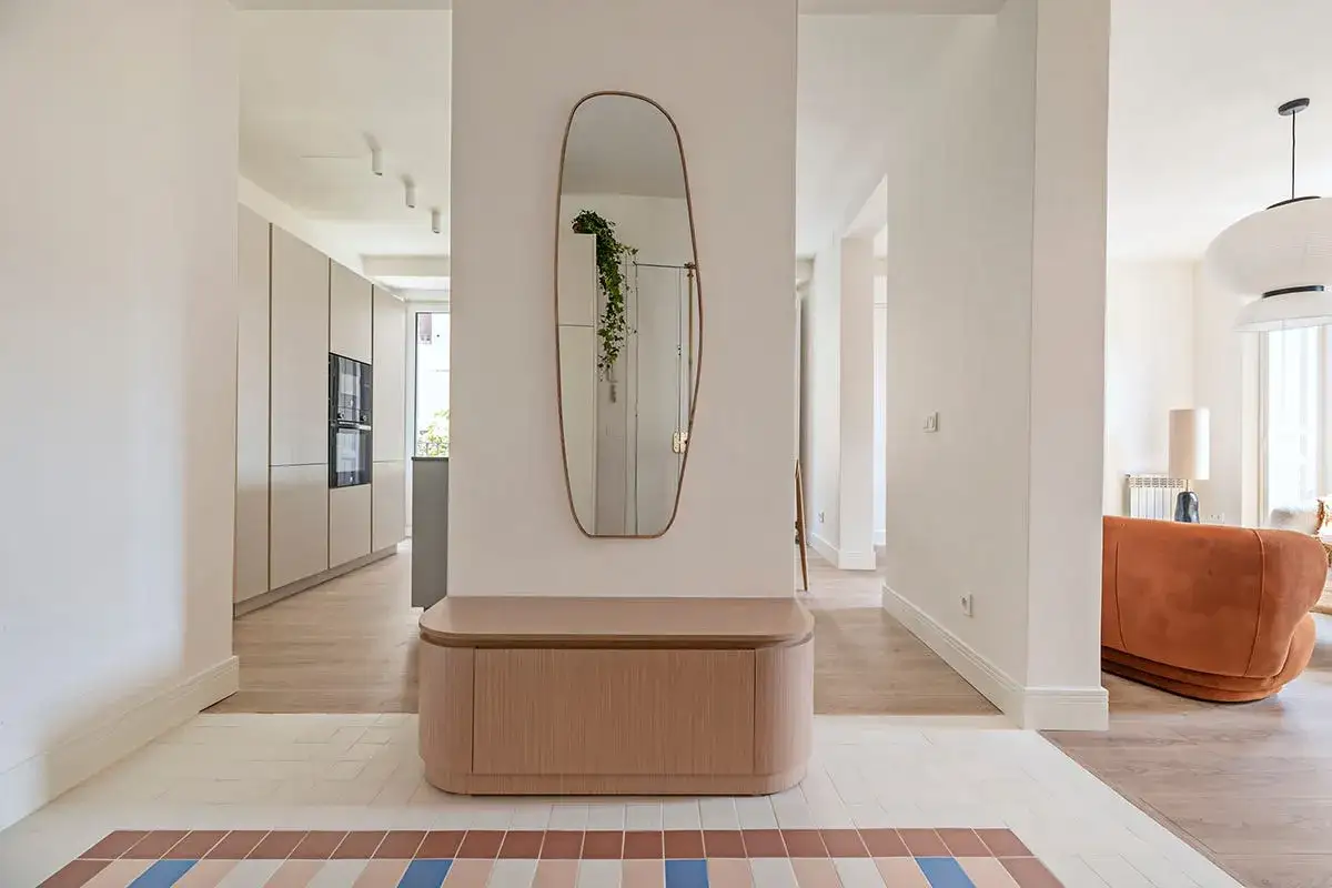 Entrada salón recibidor integrado con banco de madera, espejo orgánico y suelo de baldosas.