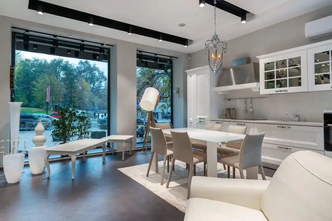 Espacio moderno de cocina salón comedor de 30 m2 con mesa blanca, sillas beige, sofá blanco y grandes ventanales.