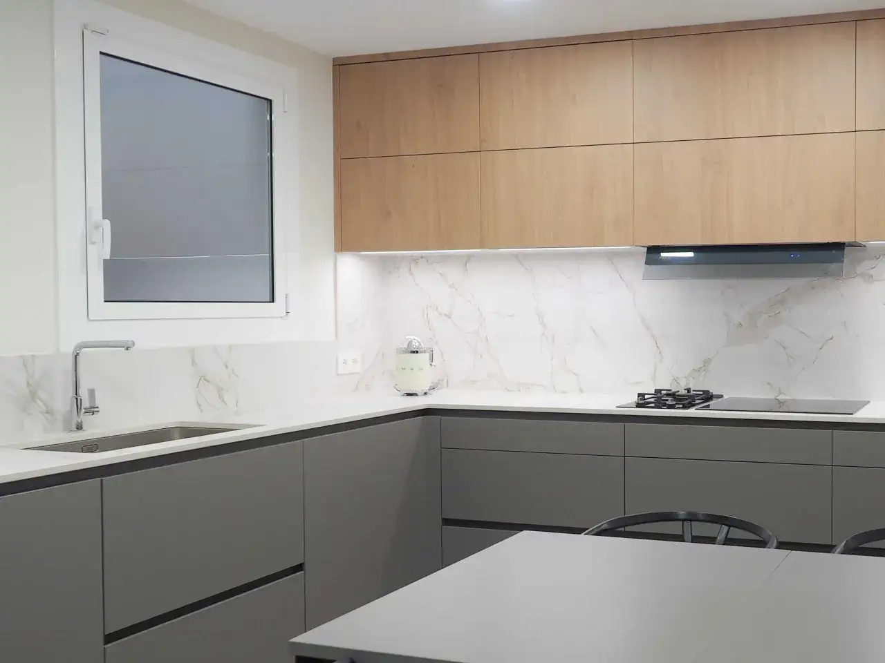Cocina moderna con gabinetes grises y de madera, encimeras de mármol y electrodomésticos integrados. Un proyecto para renovar cocina con estilo.