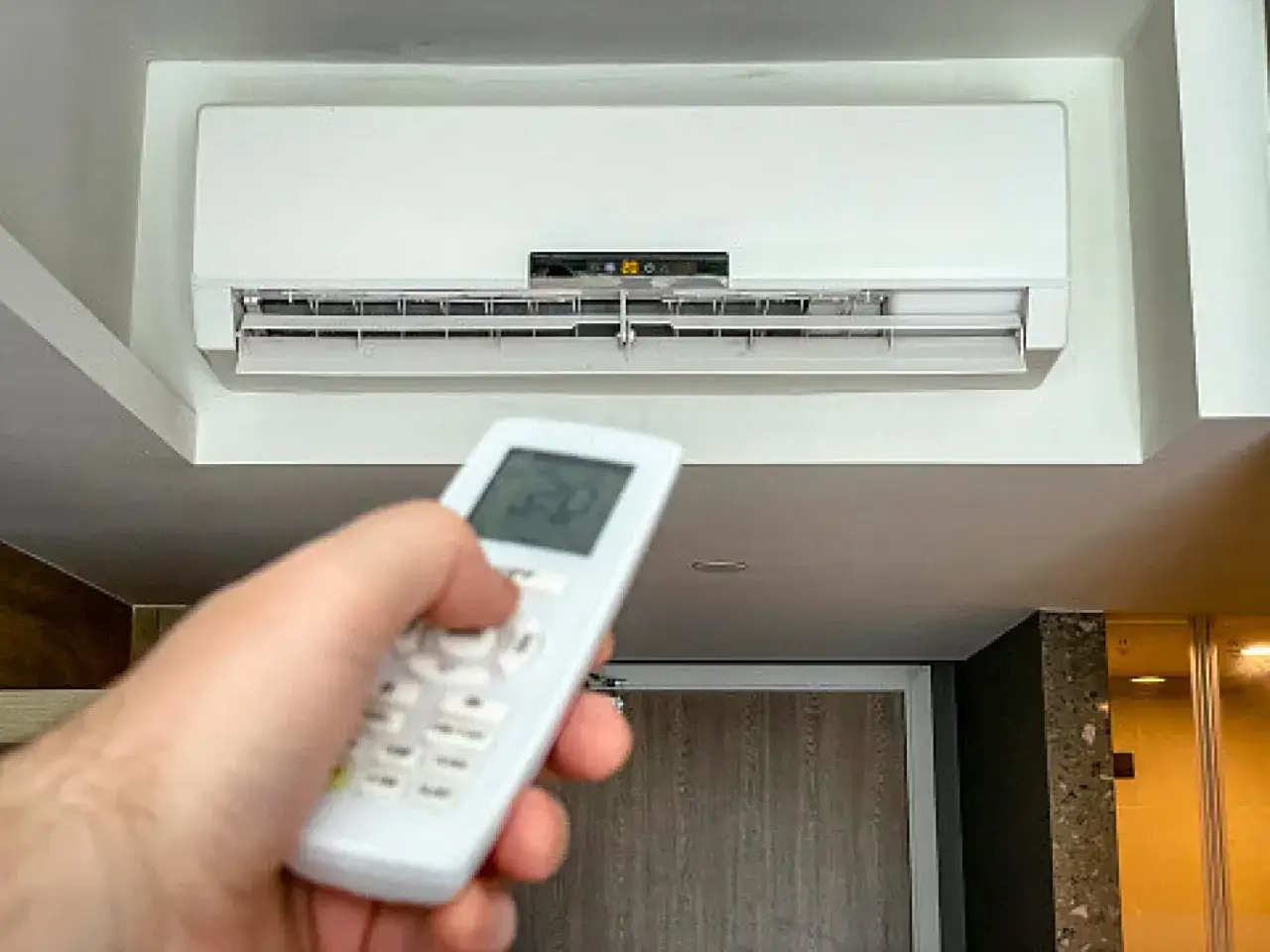 Mano ajustando la temperatura del aire acondicionado a 20 grados con el control remoto.