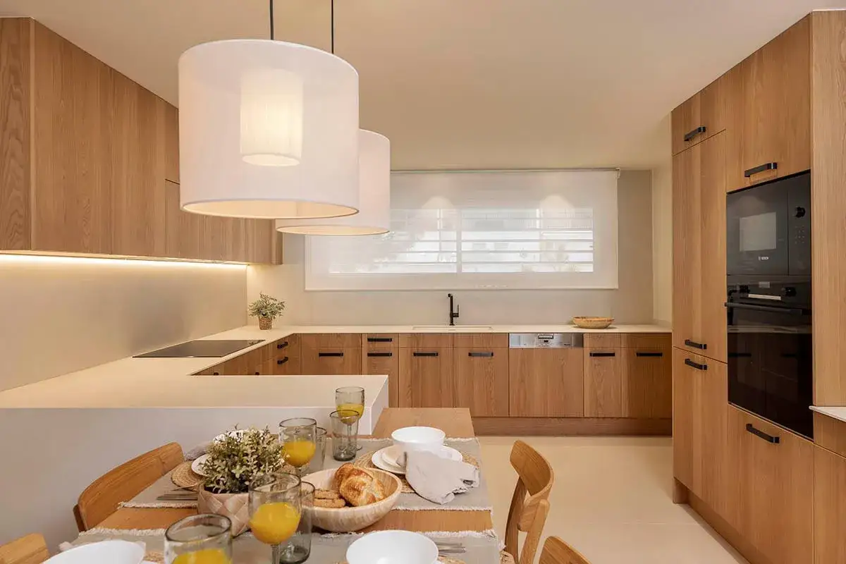 Elegantes diseños de cocinas con gabinetes de madera clara, encimeras blancas y una mesa lista para el desayuno.