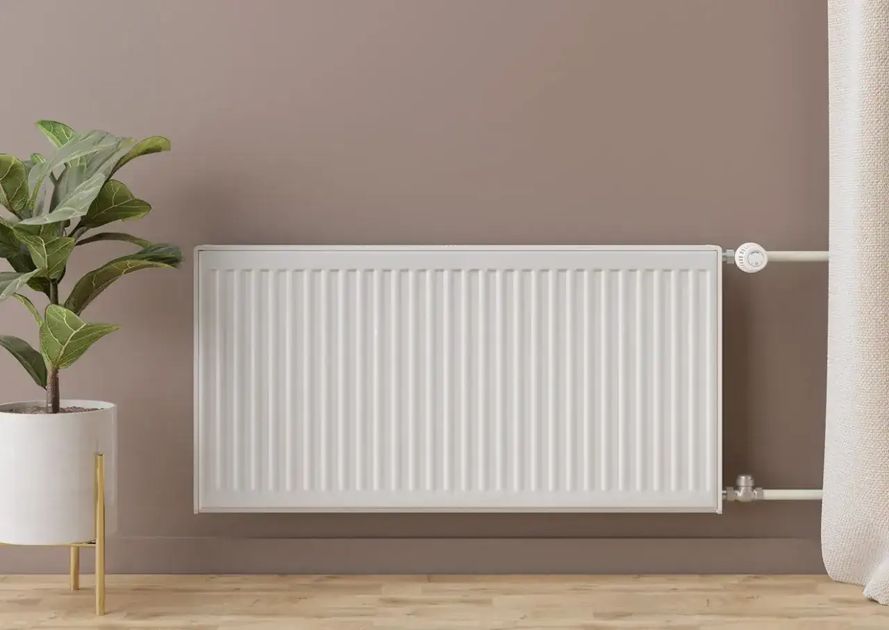 Radiador blanco moderno junto a una planta, ideal para un hogar con radiadores más eficientes y un ambiente acogedor.
