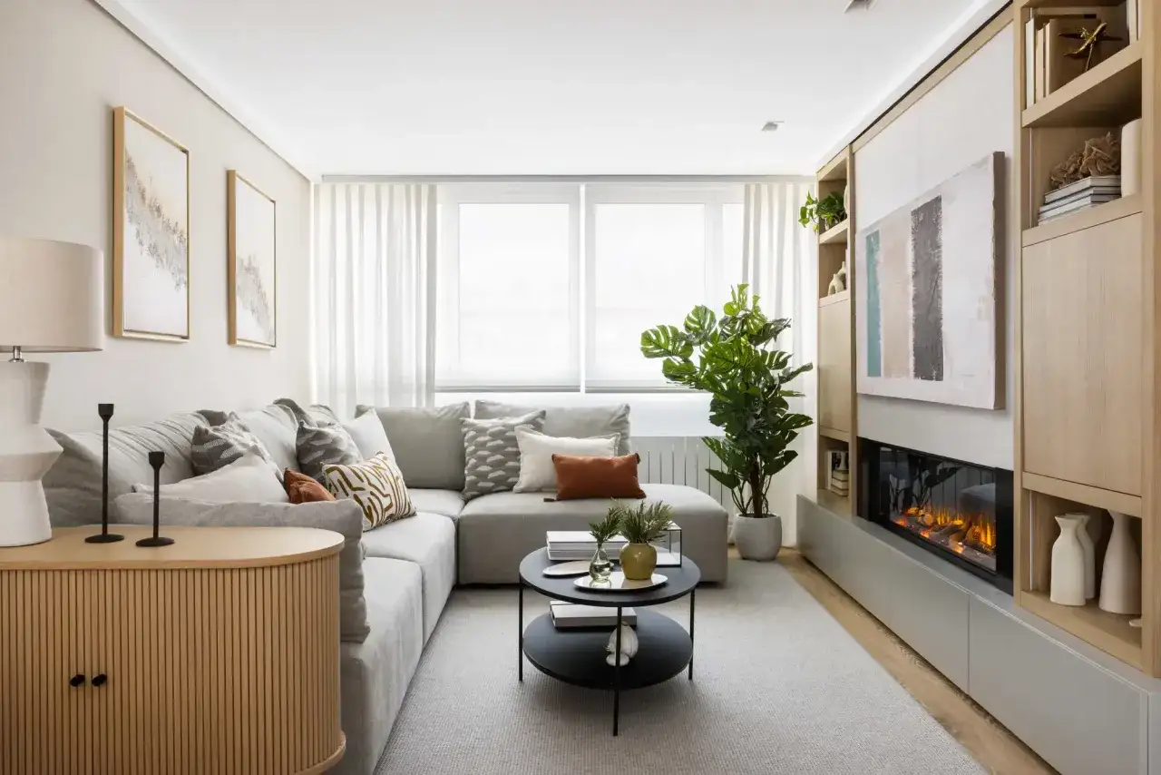 Salón moderno con sofá modular gris, mesa de centro negra y chimenea. Muebles que se transforman para optimizar el espacio.