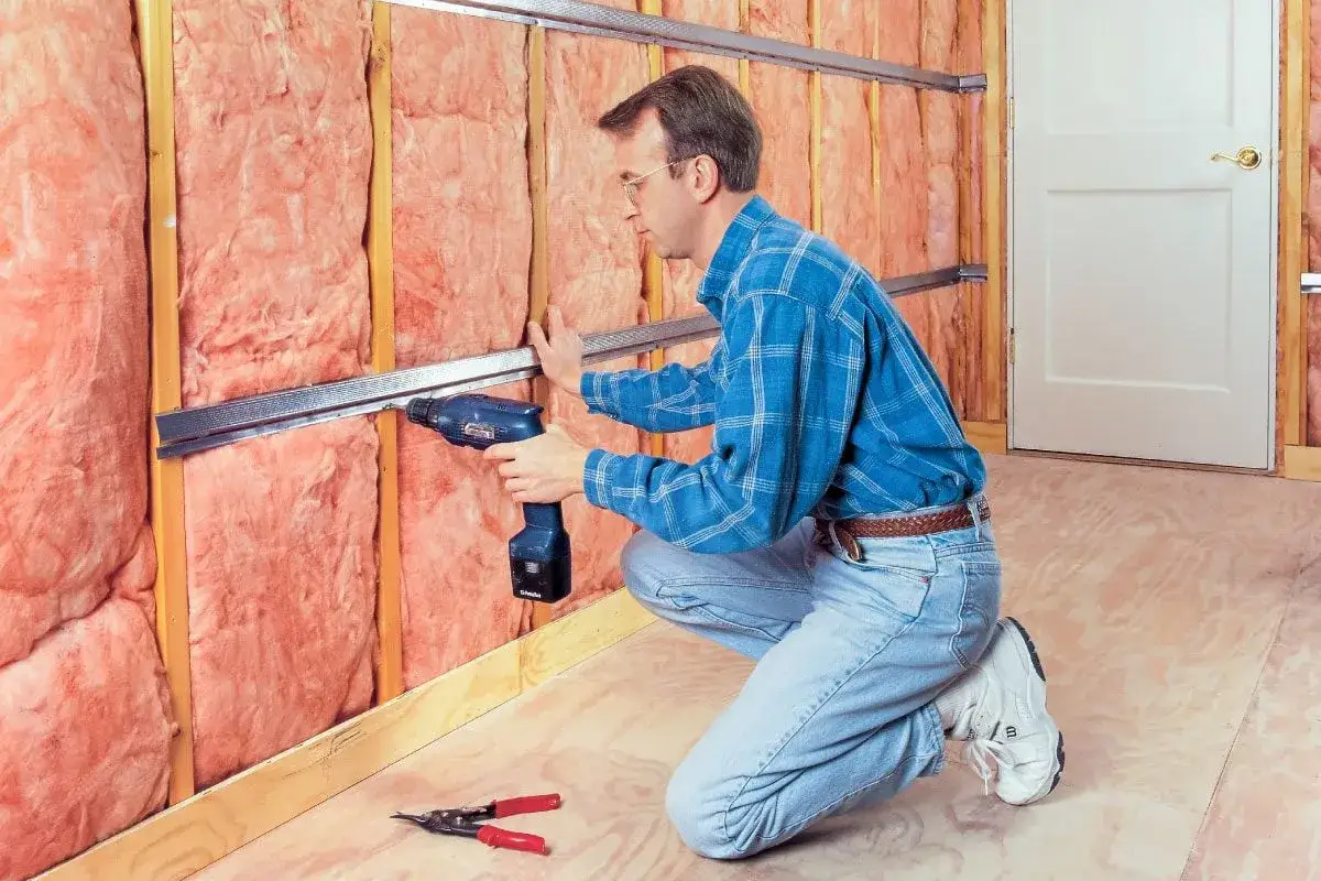 Hombre instala perfiles metálicos para insonorizar habitación con aislamiento rosa.