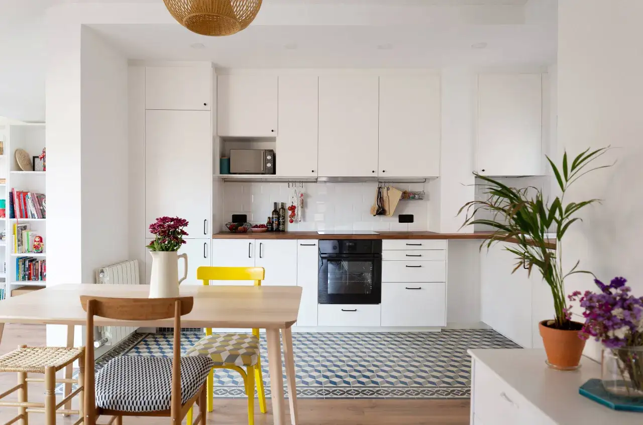 Cocina moderna con suelo hidraulico de rombos azules y blancos, muebles blancos y mesa de madera.