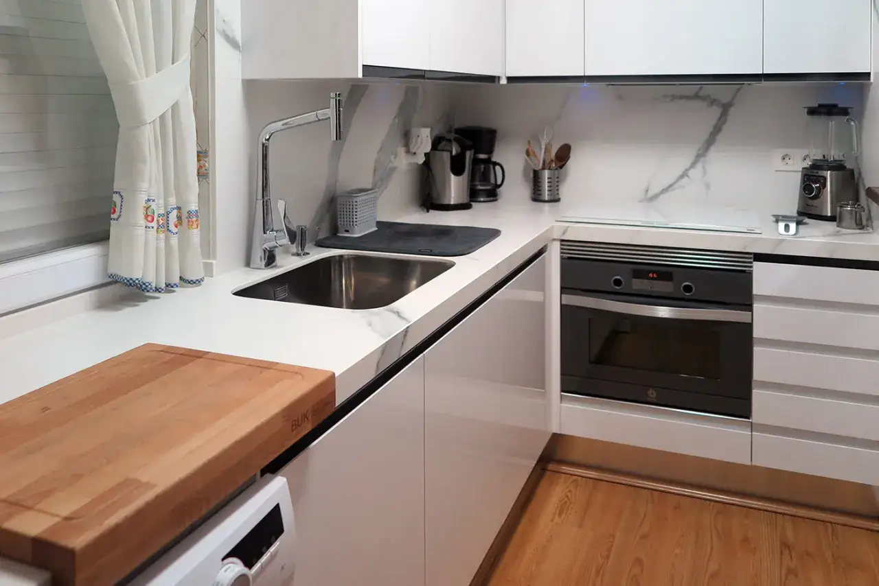 Cocina moderna con encimera blanca, fregadero, horno y tabla de cortar. Ideas diseño cocina minimalista y funcional.