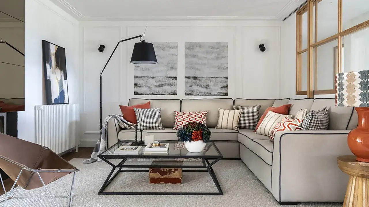Un salón moderno y acogedor con un sofá rinconera gris, cojines coloridos y una mesa de centro de cristal.