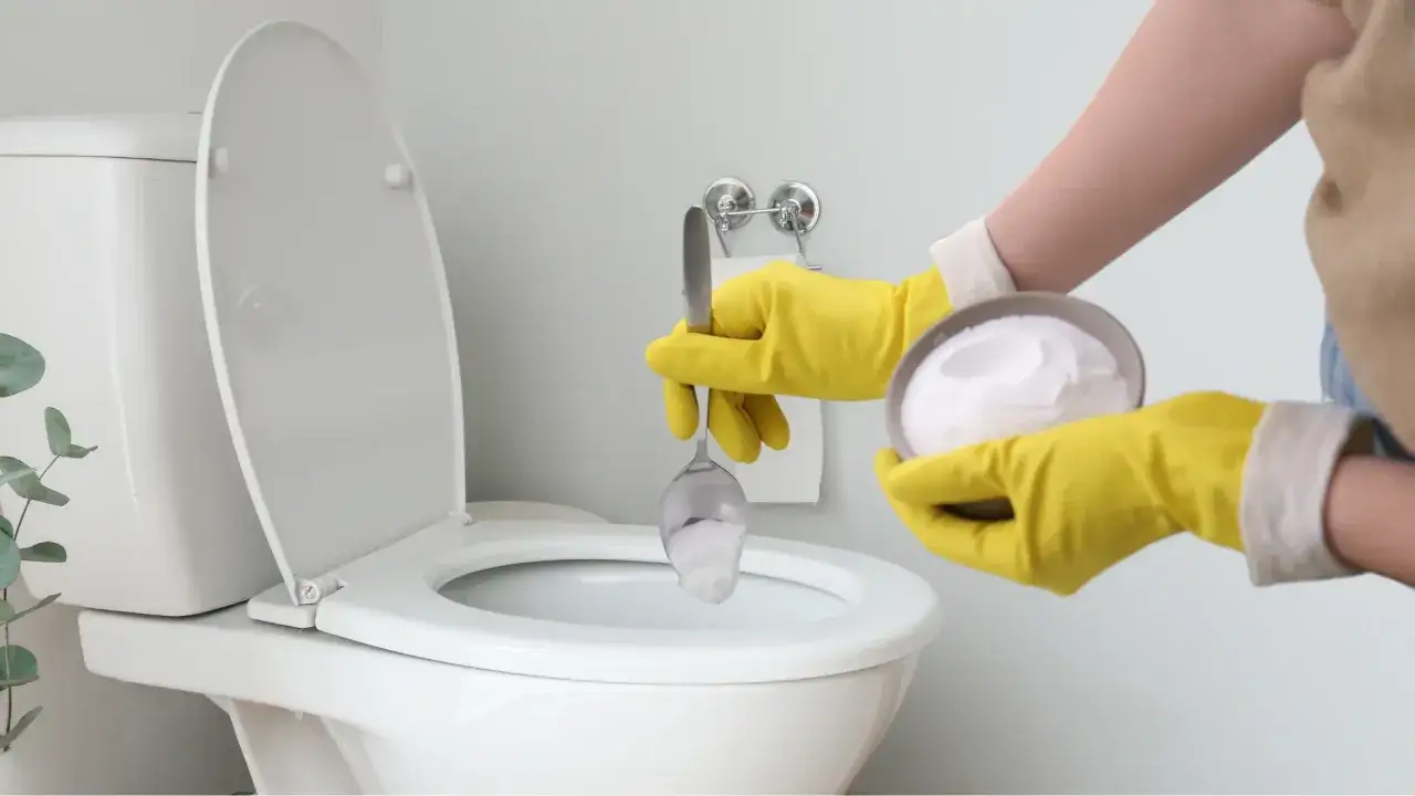 Manos con guantes amarillos vierten polvo blanco en el inodoro, un paso clave para saber como limpiar el fondo del inodoro.