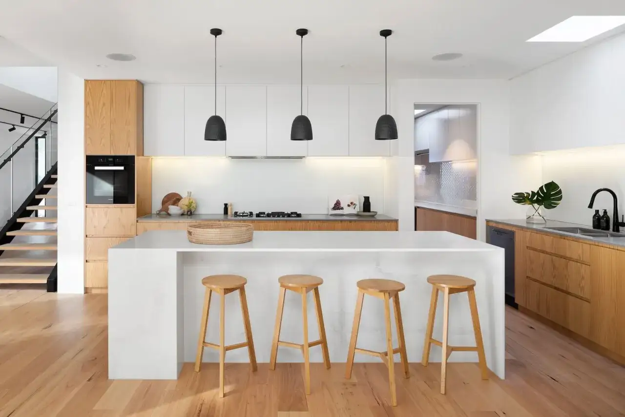 Cocina moderna con isla central y taburetes de madera. Una escalera de diseño a la izquierda. Ideas para como distribuir una cocina funcional y elegante.