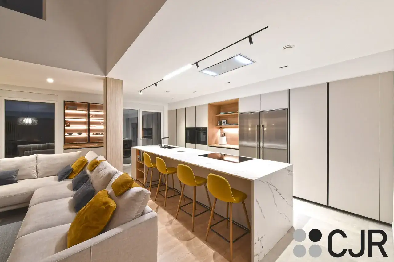 Moderna cocina abierta con isla central, taburetes amarillos y un gran sofá en forma de L.