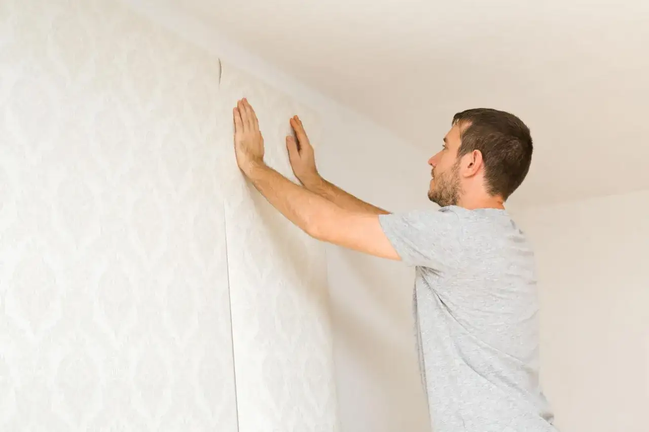 Hombre colocando papel tapiz con un patrón floral en una pared.