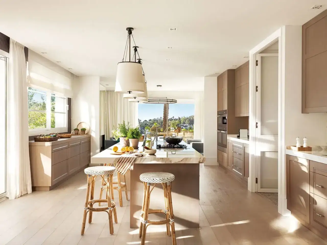 Cocina luminosa con isla central, taburetes de mimbre y vistas al exterior. Ideas para como diseñar una cocina moderna y funcional.