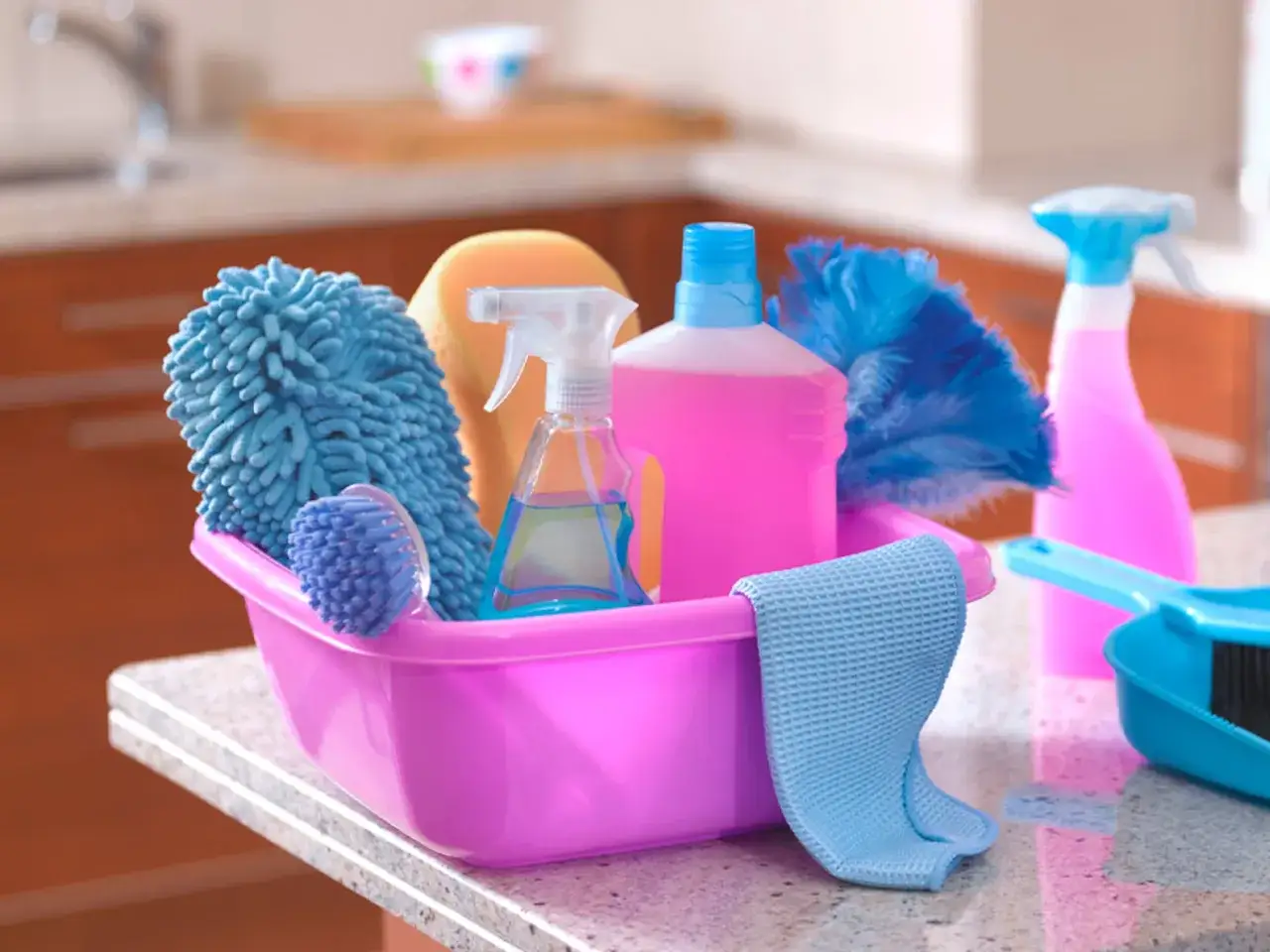 Cesta rosa con 25 productos de limpieza del hogar: esponja, cepillo, plumeros, botellas de spray y paño.