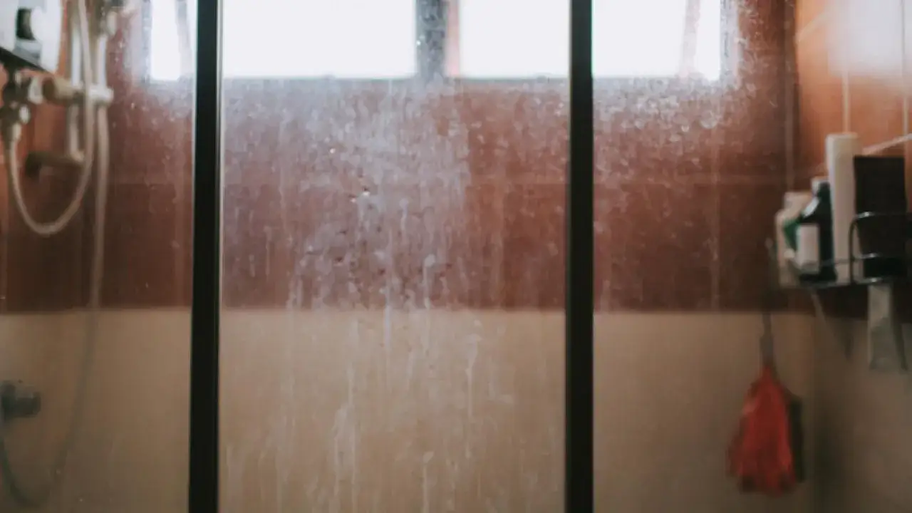 Mampara de ducha con marcas de agua y jabón, lista para la limpieza.