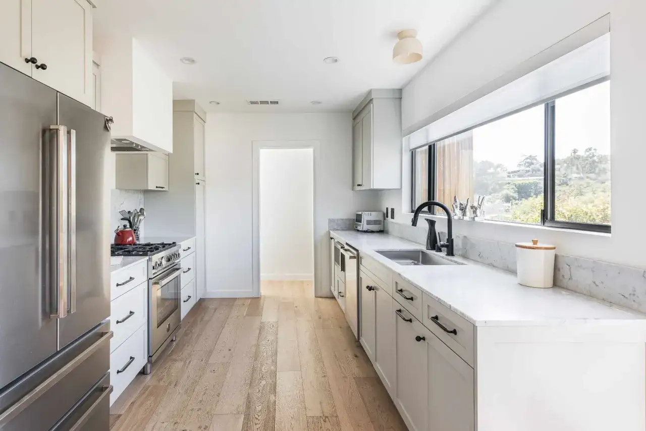 Cocina alargada con electrodomésticos de acero inoxidable, encimeras de mármol y gabinetes blancos. Perfecta para saber cómo distribuir una cocina alargada.