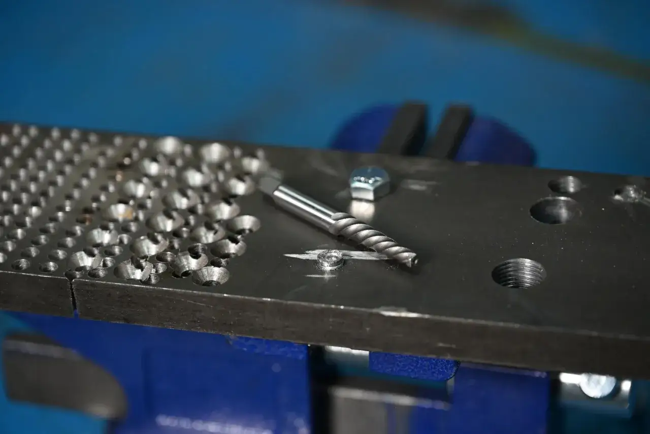 Herramienta para quitar un tornillo pasado de rosca en metal. Tornillo dañado y extractor en una placa metálica sujeta en un tornillo de banco.