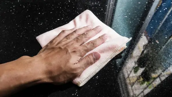 Mano limpiando una superficie de mármol negro con un paño rosa.