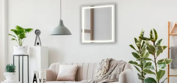 Un espejo iluminado sobre un sofá beige, con plantas y un reloj. Ideas de donde colocar espejos en el salón para ampliar el espacio.