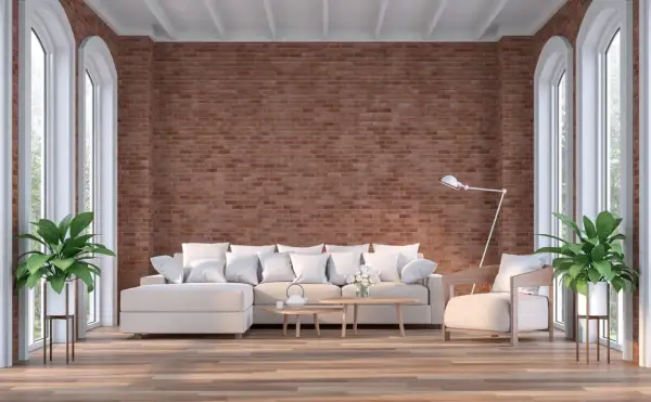 Un salón moderno con una imponente pared de ladrillo visto, sofá blanco, sillón y plantas verdes.