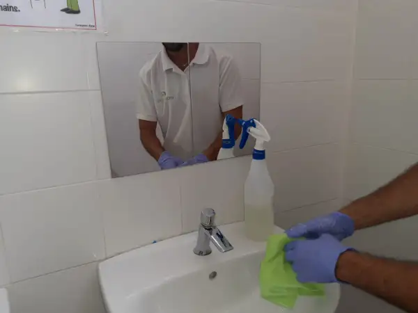 Man con guantes limpia lavabo con paño verde. Spray de limpieza cerca. Aprende como limpiar azulejos baño.
