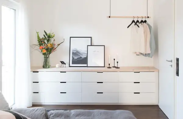 Ideas para decorar cómoda dormitorio matrimonio: ramo de flores, cuadros, velas y ropa colgada.