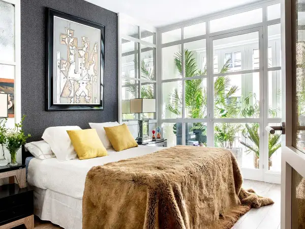 Dormitorio de matrimonio moderno con manta peluda y arte abstracto. Las ultimas tendencias en decoracion de dormitorios de matrimonio se reflejan en la luz natural y las plantas.