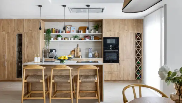 Cocina moderna con armarios de madera clara, isla central con taburetes y estanterías decoradas. Ideal para inspiración de decoracion cocinas.
