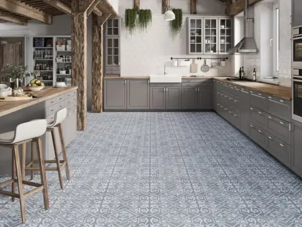 Cocina moderna con suelo hidráulico de diseño geométrico en tonos grises y blancos. Muebles de cocina grises, encimera de madera y barra americana con taburetes.
