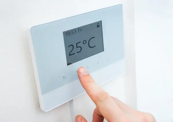 Un dedo ajusta la temperatura en un termostato digital que muestra 25°C.