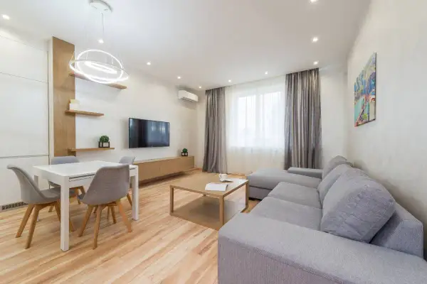 Elegante salón con sofá gris, mesa de comedor blanca y detalles en madera. Los colores del salón crean un ambiente acogedor y moderno.