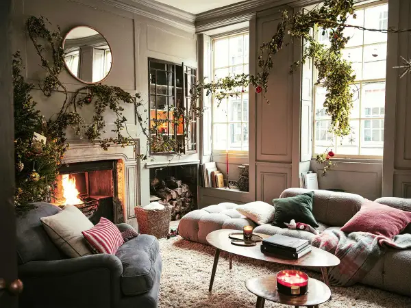 Acogedor salón decorado de Navidad con chimenea encendida, árbol y guirnaldas verdes colgando.