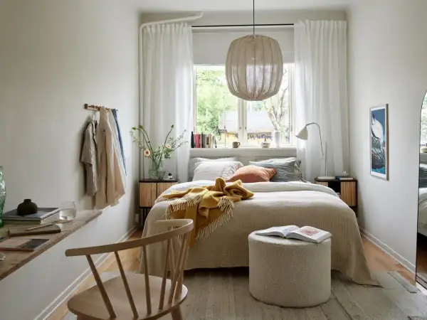 Acogedora cama bajo ventana, con manta amarilla y cojines. Ideas para un dormitorio luminoso y funcional.
