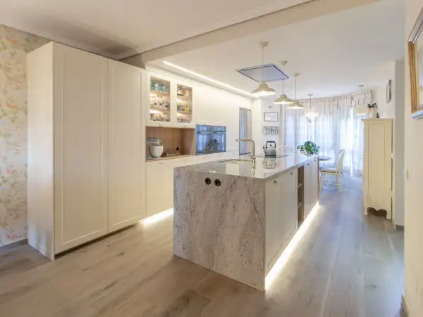 Cocina moderna con isla central de granito, gabinetes blancos y suelo de madera. Una guía visual sobre como distribuir una cocina funcional y elegante.