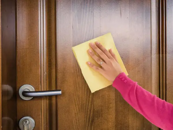 Mano con paño amarillo limpiando puertas de madera barnizadas muy sucias.