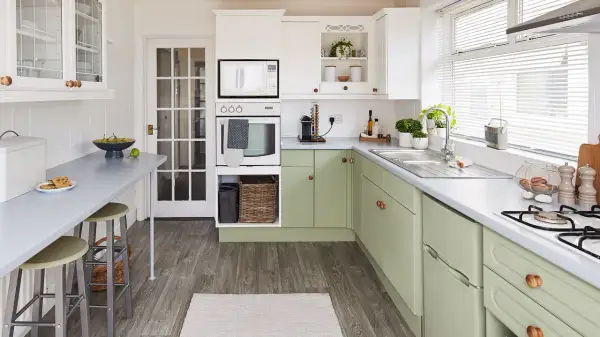 Cocina renovada con gabinetes verdes, encimeras grises y electrodomésticos blancos. Un espacio luminoso y funcional para tu reforma cocina.