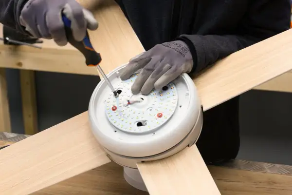 Manos enguantadas atornillan el motor de un ventilador de techo.