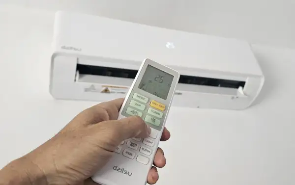 Mano ajustando el control remoto del aire acondicionado para cambiar la temperatura. La pantalla muestra 25.5°C.