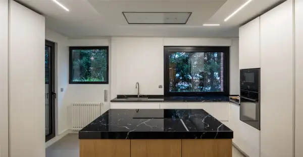 Moderna cocina con isla central de mármol negro y madera. Encimeras a juego, electrodomésticos integrados y grandes ventanales.