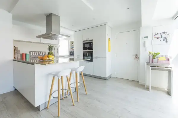 Cocinas modernas blancas con isla central, taburetes y electrodomésticos integrados. Un espacio luminoso y funcional.