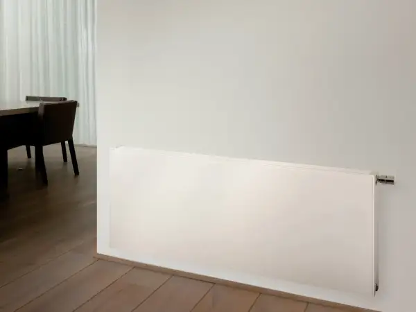 Radiadores de alta temperatura blancos, modernos y discretos, instalados en una pared junto a un suelo de madera y una mesa con sillas.