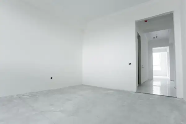 Habitación vacía con paredes blancas y suelo de cemento. El yeso aguanta el calor, preparándose para un nuevo hogar.