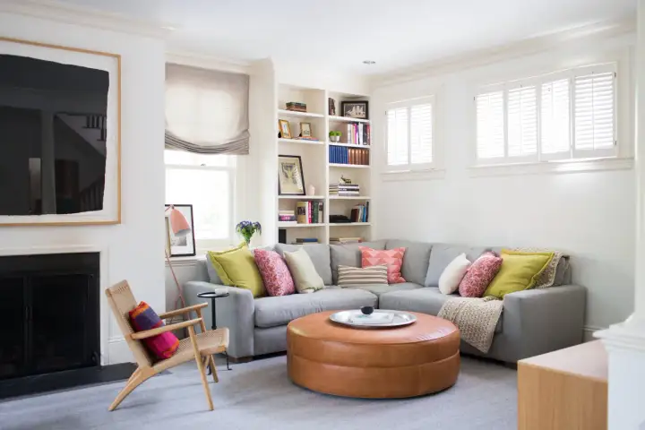 Un salón moderno y acogedor con un sofá rinconera gris, cojines coloridos y un puf de cuero. Ideal para decorar salón con sofá rinconera.